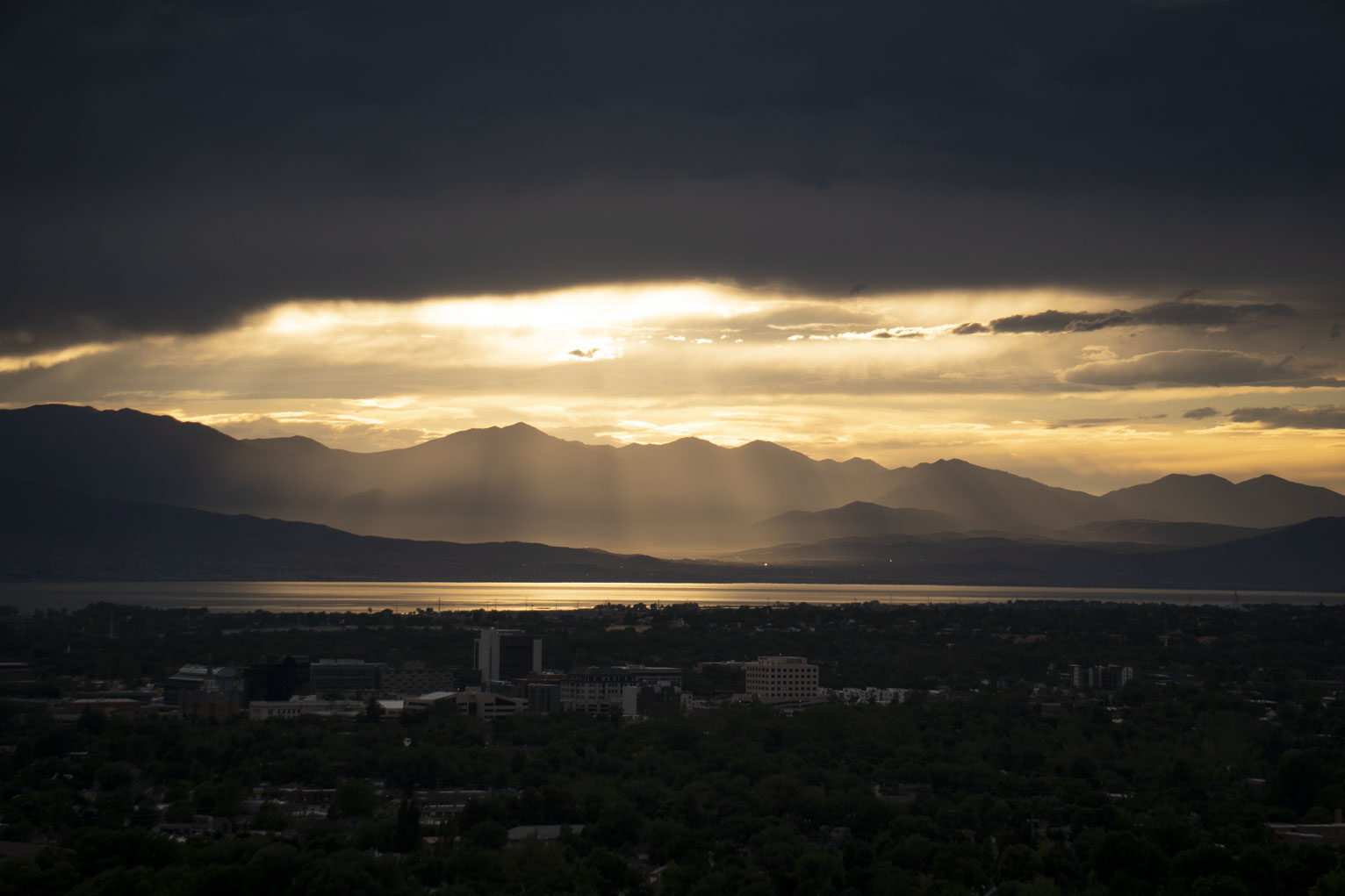 The setting sun just above a gap in the clouds spills sunrays out onto the various slopes of the mountains to the west